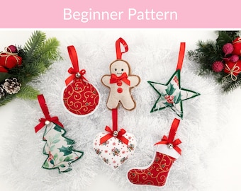 Puede incluir: Seis adornos navideños de tela que incluyen un hombre de jengibre, una estrella, un corazón, un calcetín, un árbol y una bola. Cada adorno tiene un lazo de cinta roja, una pequeña campana plateada y un lazo rojo. Texto "Beginner Pattern".