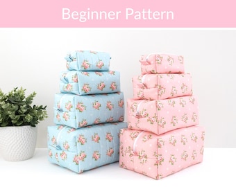 May include: Two stacks of four rectangular zippered pouches in varying sizes. The left stack is light blue with a pink floral and white polka dot pattern. The right stack is light pink with a matching floral and white polka dot pattern. Text reads Beginner Pattern.