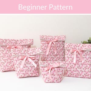 May include: Five fabric pouches in varying sizes featuring a pink floral pattern with small white and dark brown flowers. Each pouch has a folded top edge and a light pink satin ribbon tied in a bow at the center. The text Beginner Pattern is visible.