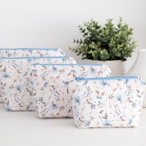 Four beginner zip pouches in soft blue and pink floral fabric, arranged in graduated sizes from large to small on a white table with a plant and white pot.