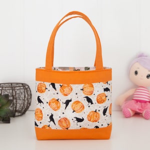May include: A small orange tote bag with a white fabric lining featuring a pattern of black crows and orange pumpkins. The bag has two orange handles.