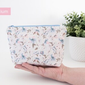 Medium floral zip pouch held in one hand beside a potted plant, labelled Medium.