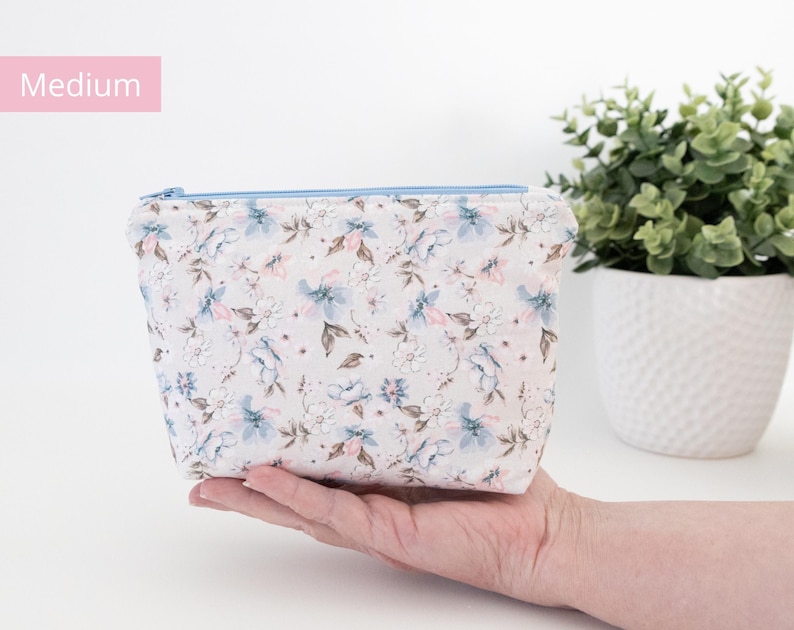 Medium floral zip pouch held in one hand beside a potted plant, labelled Medium.
