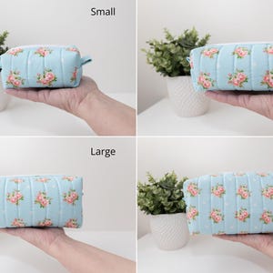 May include: A light blue quilted pouch featuring a repeating pattern of pink roses and white polka dots, shown in four sizes labeled Small, Medium, Large, and Extra Large. The rectangular pouch has a zippered top and a soft, padded fabric texture.