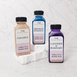 May include: Three square plastic bottles of sulfate-free bubble bath with black caps. The labels read NMJ Handmade Creations, with scents Coconut, Midnight Romance, and Lavender & Rosemary. Each bottle contains 8 oz (226 g) of liquid product.