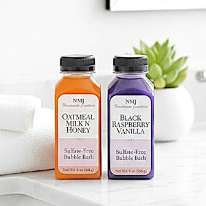 May include: Two bottles of sulfate-free bubble bath, one orange and one purple, with black caps. The orange bottle is labeled "Oatmeal Milk N Honey," and the purple bottle is labeled "Black Raspberry Vanilla." Each bottle contains 8 oz (236 g).