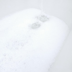 White bathtub filled with rich, fluffy foam created by NMJ Handmade Creations sulfate-free bubble bath. Thick layers of soft bubbles cover the water surface, showing the luxurious lather effect in a bright, clean setting.