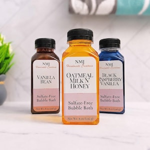 May include: Three square plastic bottles with black caps containing bubble bath. The labels read NMJ Handmade Creations, with scents Vanilla Bean, Oatmeal Milk N' Honey, and Black Raspberry Vanilla. Each bottle states Net Wt. 8 oz (226 g).