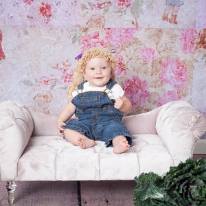 A baby wearing a handmade Halloween hat designed to look like baby doll hair from a Cabbage Patch Kid. The crocheted hat features textured yarn mimicking doll-like hair, giving the baby a charming, doll-inspired appearance