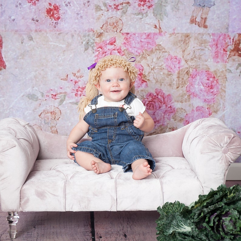 A baby wearing a handmade Halloween hat designed to look like baby doll hair from a Cabbage Patch Kid. The crocheted hat features textured yarn mimicking doll-like hair, giving the baby a charming, doll-inspired appearance