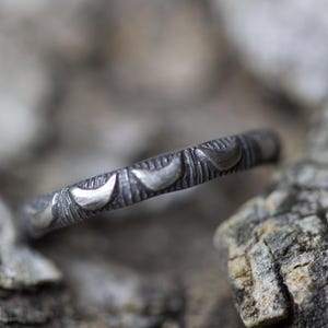 May include: A silver ring with a textured band and crescent moon designs.