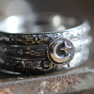May include: A silver ring with a crescent moon and star design. The ring is made of multiple bands with intricate details.