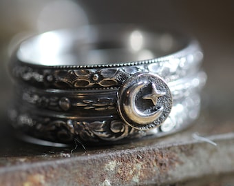 May include: A silver ring with a crescent moon and star design. The ring is made of multiple bands with intricate details.