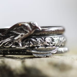 May include: A set of four silver rings with intricate designs. The top ring features a bird, the second ring has a floral design, the third ring has a feather design, and the bottom ring has a textured design.