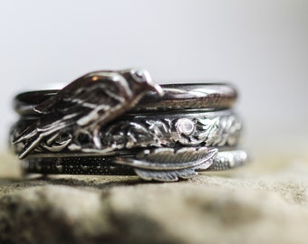 May include: A set of four silver rings with intricate designs. The top ring features a bird, the second ring has a floral design, the third ring has a feather design, and the bottom ring has a textured design.