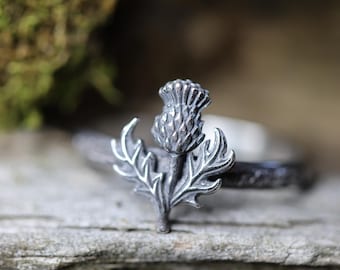 May include: A silver ring with a detailed thistle design. The thistle is a traditional symbol of Scotland.
