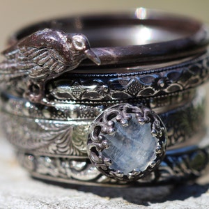 May include: A stack of five silver rings with intricate designs. The top ring features a small bird with a clear gemstone in the center.