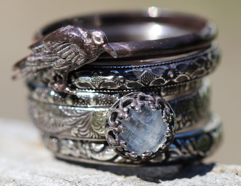 May include: A stack of five silver rings with intricate designs. The top ring features a small bird with a clear gemstone in the center.