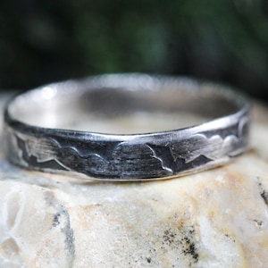 May include: A silver ring with a textured, cloud-like design. The ring is made of metal and has a brushed finish.