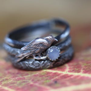 Peut inclure: Une bague en argent avec un motif d'oiseau détaillé et une pierre précieuse bleu clair. La bague est empilée avec deux autres bandes en argent.