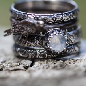 May include: A stack of silver rings with intricate designs. The top ring features a bird design, and the bottom ring has a clear stone.