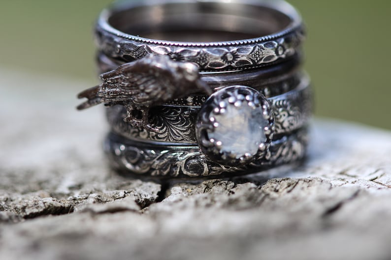 May include: A stack of silver rings with intricate designs. The top ring features a bird design, and the bottom ring has a clear stone.