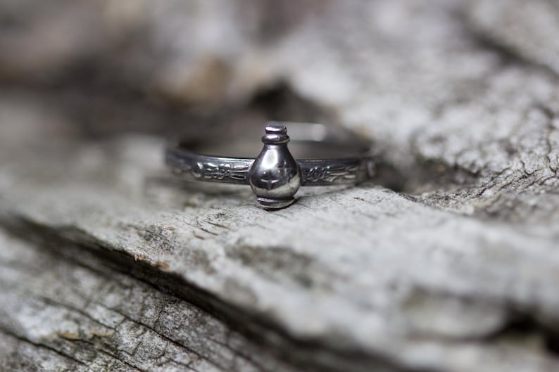 May include: A silver ring with a detailed design featuring a small bottle charm.