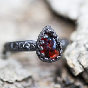 May include: A silver ring with an ornate design and a teardrop-shaped red gemstone.