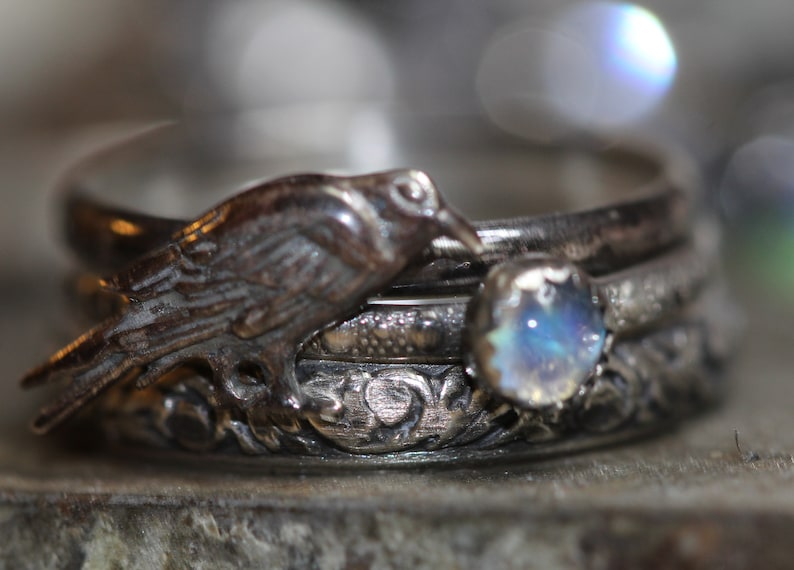 Puede incluir: Un anillo de plata con un dise&ntilde;o de p&aacute;jaro y una piedra de luna. El anillo est&aacute; hecho de cuatro bandas.