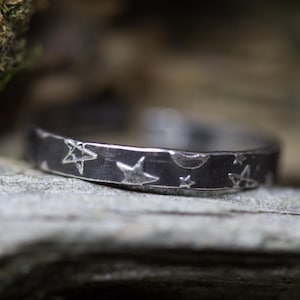 May include: A silver ring with a black oxidized finish and a design of stars and a crescent moon.