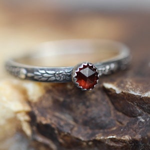 May include: A silver ring with a red gemstone set in the center. The band is decorated with a floral design.