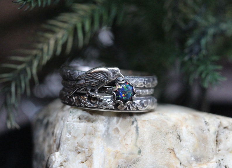 Puede incluir: Un anillo de plata con una piedra de &oacute;palo negro y un dise&ntilde;o de p&aacute;jaro detallado. El anillo est&aacute; formado por tres bandas.