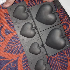 Op de afbeelding: Een set van vijf zwarte hartvormige mallen voor het maken van chocolade of andere lekkernijen. De mallen zijn gemaakt van een duurzaam materiaal en zijn gemakkelijk schoon te maken.