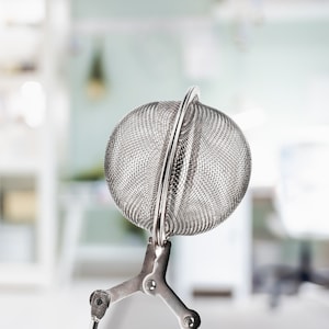 May include: A silver mesh tea infuser with a handle that has two prongs. The infuser is round and has a fine mesh.