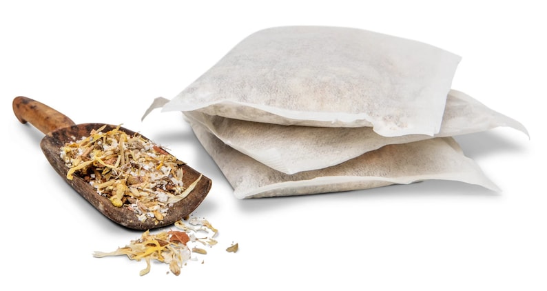 May include: A wooden scoop filled with dried herbs and flowers, with three white muslin bags of the same herbs and flowers stacked next to it.