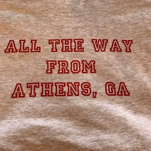 May include: Gray t-shirt with red text that reads "All the way from Athens, GA".