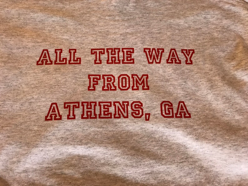 May include: Gray t-shirt with red text that reads "All the way from Athens, GA".