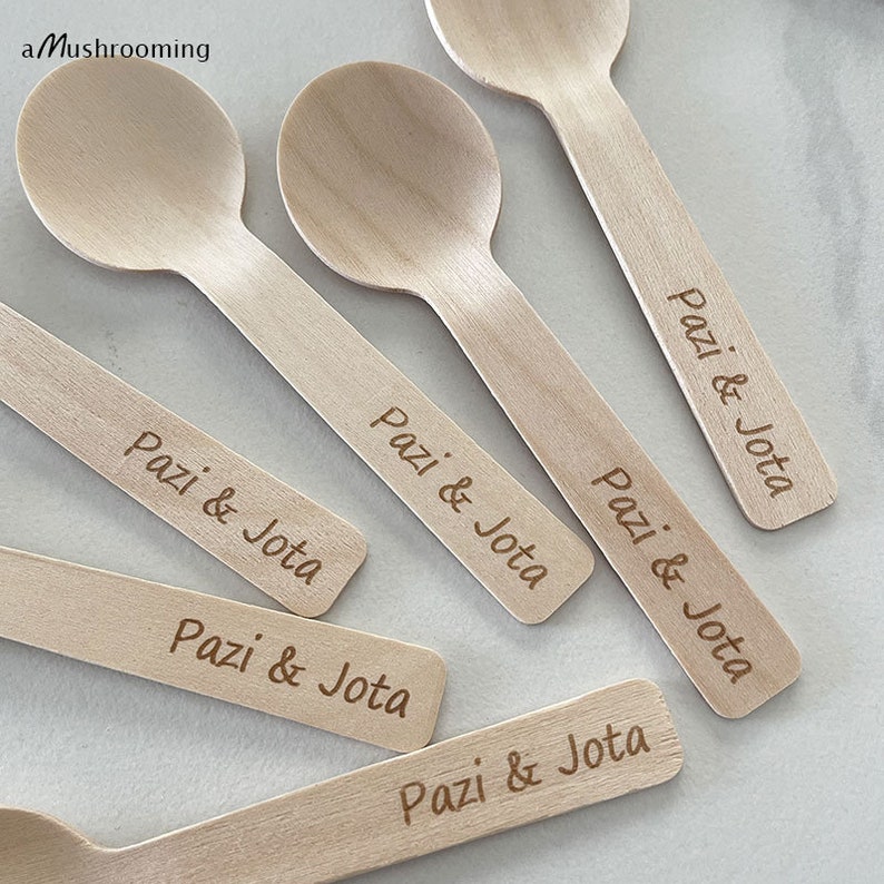 May include: A selection of wooden spoons and stirrers. Each spoon and stirrer is engraved with the text "Pazi & Jota". The spoons have a rounded bowl, while the stirrers are flat. The logo "a Mushrooming" is in the top left corner.