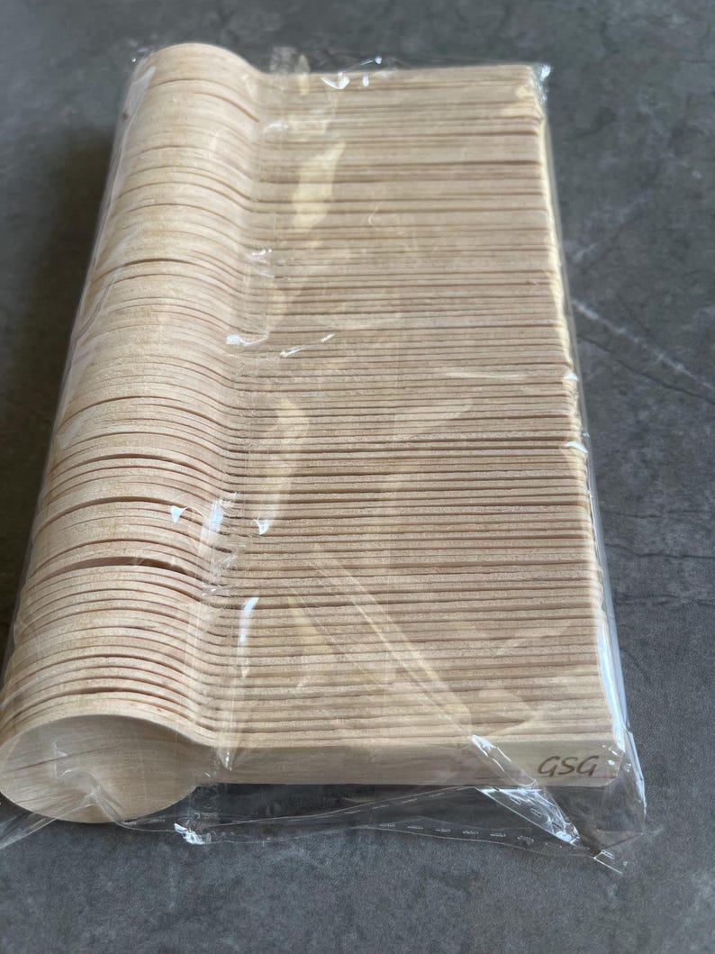 May include: A pack of disposable wooden spoons. The spoons are light brown and have a rounded bowl shape. The spoons are packaged in clear plastic. The package is rectangular and contains many spoons. The spoons are made of wood.