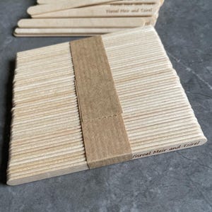 May include: A stack of light-colored wooden craft sticks bundled together with a brown paper band. Each stick features the engraved text Yisroel Meir and Tzirel. The sticks are arranged in a neat rectangular pile with rounded ends.