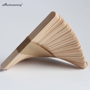 May include: A stack of light-colored wooden craft sticks arranged in a fan shape and secured with a brown paper band. The text aMushrooming is visible in the upper left corner. The sticks have rounded ends and a smooth, natural wood grain finish.