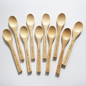 Può includere: Una collezione di cucchiai di legno color chiaro. Ogni cucchiaio ha un manico lungo e una ciotola arrotondata. Il testo "ATONWB The Bogopisky Family" è stampato sul manico di ogni cucchiaio.