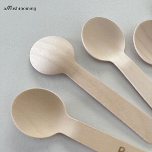 May include: A collection of wooden spoons, each with a rounded bowl and a slender handle. The spoons are made from light-coloured wood and are arranged at an angle. The text "a Mushrooming" is visible in the top left corner.