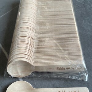 May include: A bundle of wooden spoons in a clear plastic wrapper. One spoon is shown separately, with the engraved text "Eddie ❤️ Delanie". The spoons are light brown and are likely disposable.