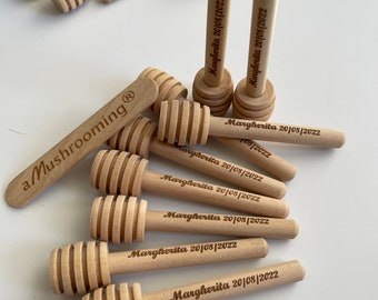 May include: A selection of light-coloured wooden honey dippers. Each dipper features a grooved head and a handle. Some handles are engraved with the text "Margherita 20/08/2022" and "a Mushrooming®".