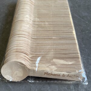 May include: A pack of disposable wooden spoons. The spoons are light brown and have a rounded bowl shape. The text "Michaela & Austin" is printed on the handle of the spoon.
