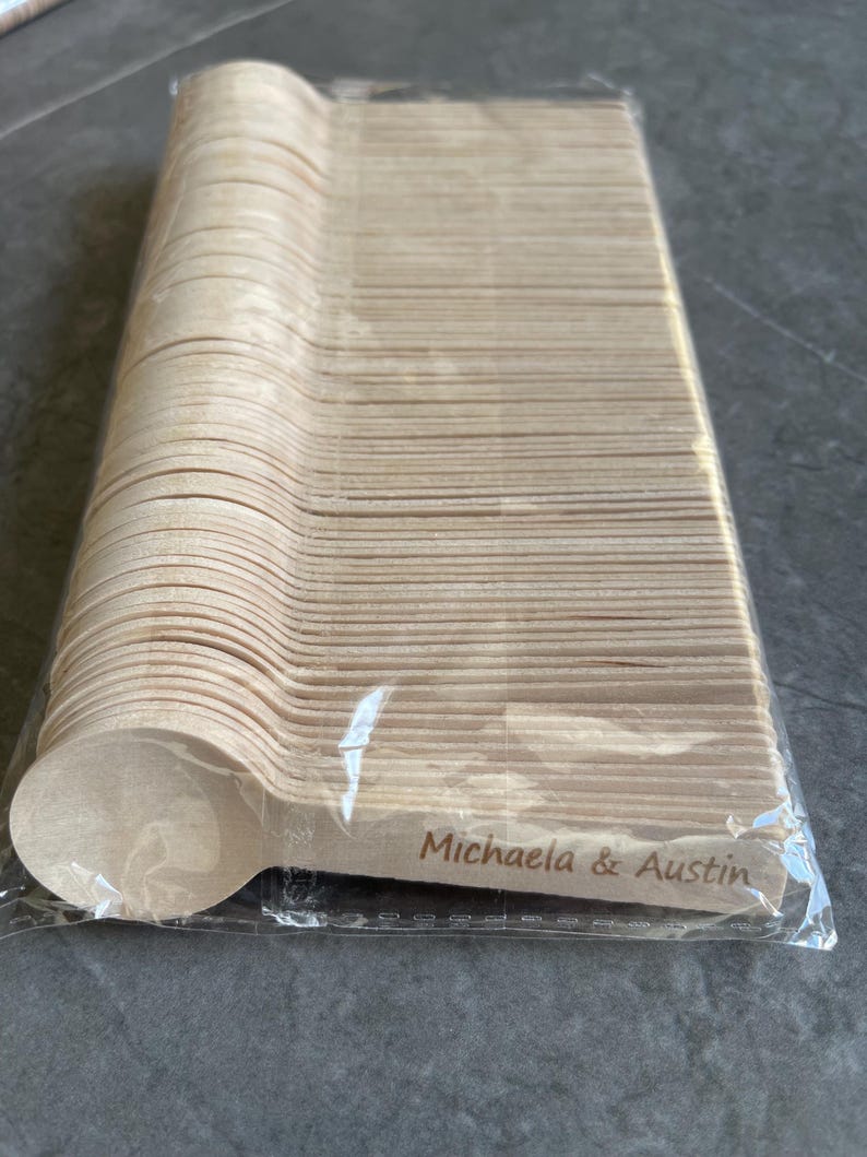 May include: A pack of disposable wooden spoons. The spoons are light brown and have a rounded bowl shape. The text "Michaela & Austin" is printed on the handle of the spoon.