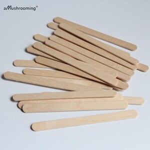 May include: A collection of light-colored wooden craft sticks with rounded ends, arranged in a scattered pile. The text aMushrooming is printed in black in the upper left corner of the image, featuring a small registered trademark symbol.