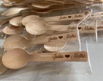 May include: A selection of small, light-coloured wooden spoons, individually packaged. Each spoon is engraved with the names "Justin" and "Mattie" separated by a heart symbol. Suitable for wedding favours or special occasions.