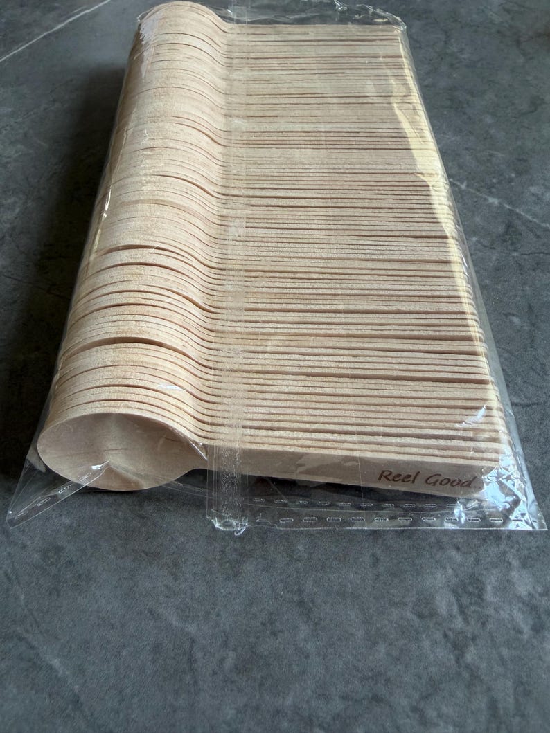 May include: A pack of disposable wooden spoons. The spoons are light brown and have a rounded bowl shape. The text "Reel Good" is printed on the side of the spoons. The spoons are packaged in a clear plastic bag.